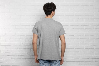 Photo of Man wearing gray t-shirt near white brick wall, back view. Mockup for design