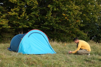 Man setting up blue camping tent near forest