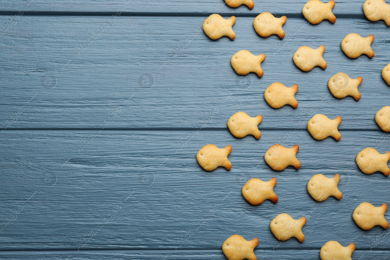 Photo of Delicious goldfish crackers on blue wooden table, flat lay. Space for text