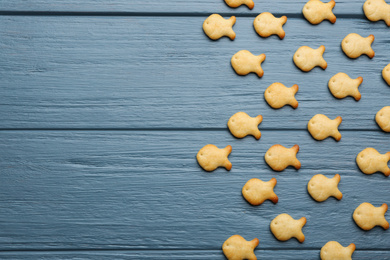 Photo of Delicious goldfish crackers on blue wooden table, flat lay. Space for text