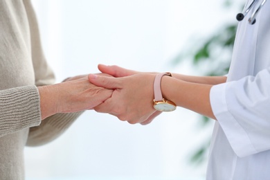 Photo of Doctor holding elderly patient hands on blurred background, closeup
