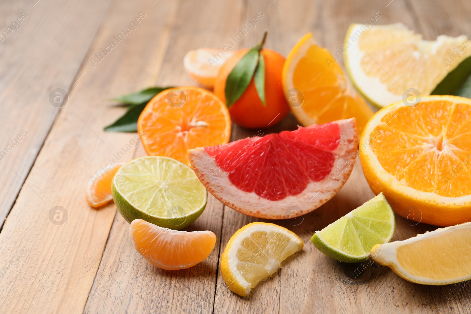 Photo of Different citrus fruits with fresh leaves on wooden table