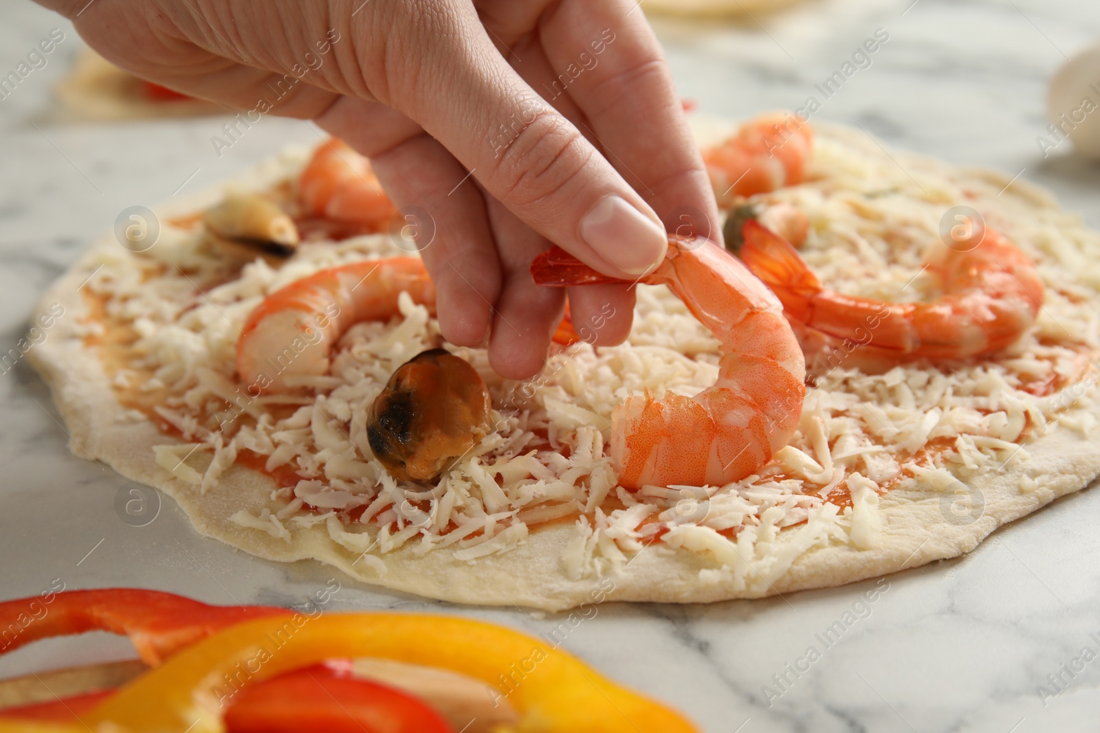 Photo of Woman adding shrimp to seafood pizza at white marble table, closeup