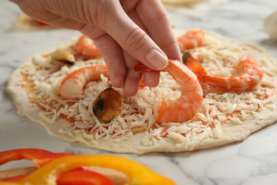 Woman adding shrimp to seafood pizza at white marble table, closeup