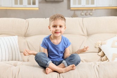 Photo of Little boy meditating on soft sofa at home