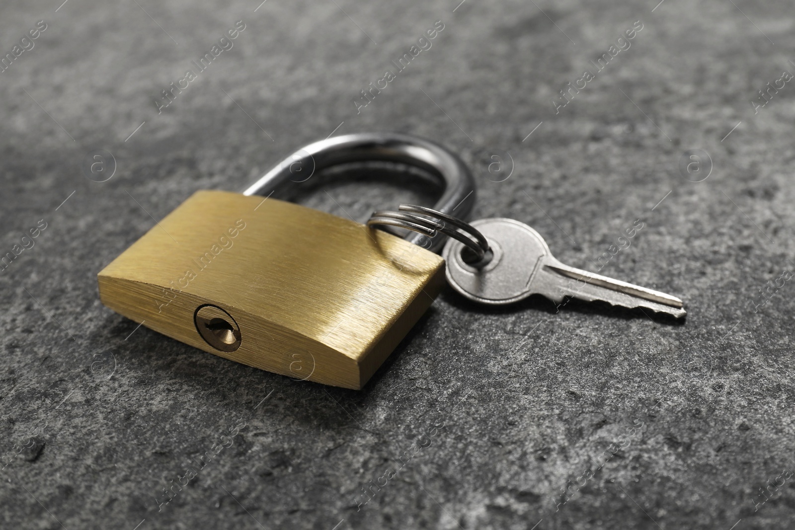 Photo of Steel padlock with key on grey table, closeup