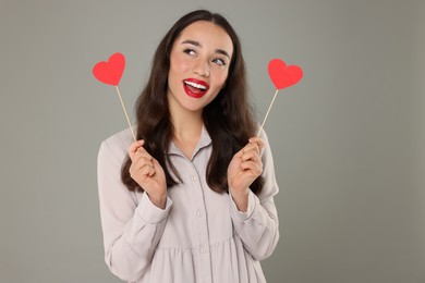 Beautiful young woman with paper hearts on grey background