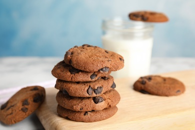 Photo of Wooden board with stack of tasty chocolate chip cookies on table