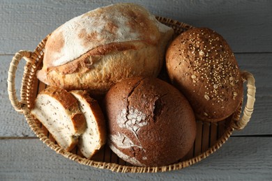 Photo of Wicker basket with different types of fresh bread on grey wooden table, top view