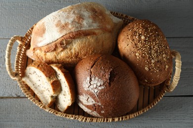 Wicker basket with different types of fresh bread on grey wooden table, top view