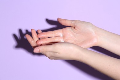 Woman applying cream on her hand against violet background, closeup