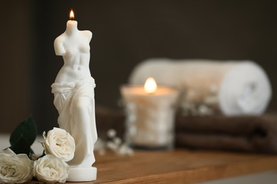 Photo of Beautiful Venus De Milo candle and white roses on wooden table in room, space for text