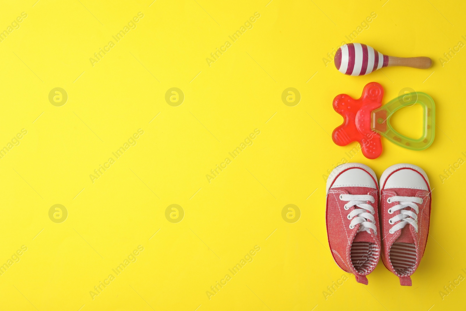 Photo of Child's shoes, toy and teether on yellow background, flat lay with space for text