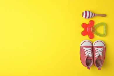 Child's shoes, toy and teether on yellow background, flat lay with space for text
