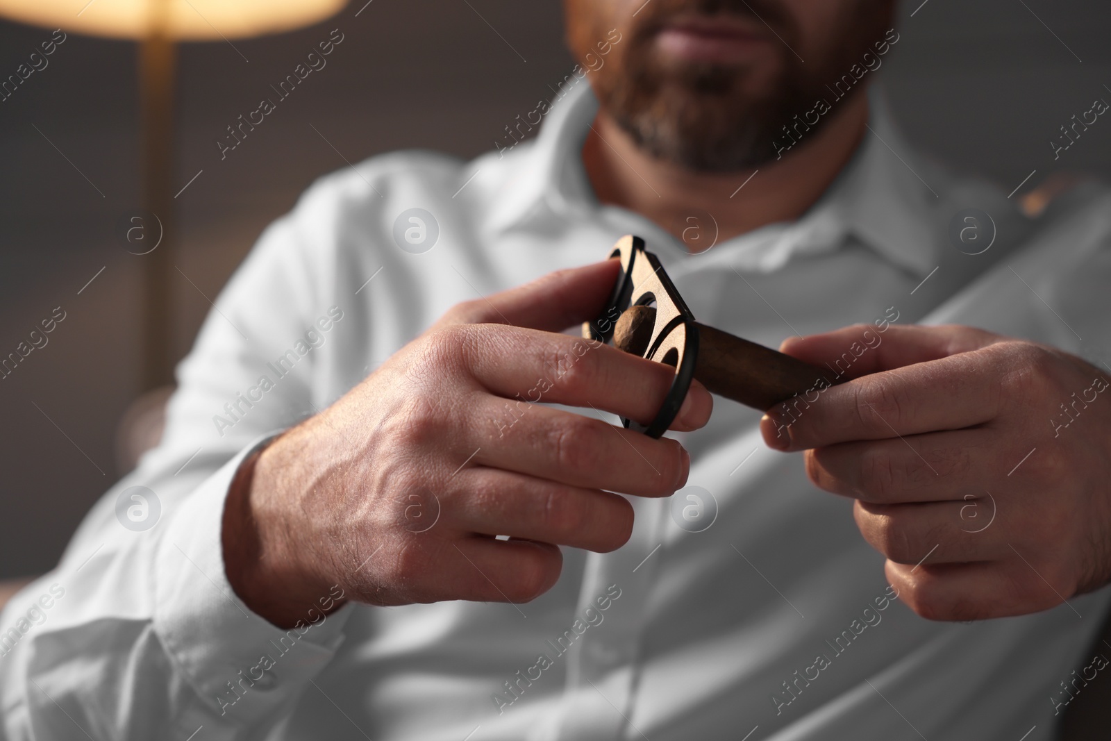 Photo of Man cutting tip of cigar at home, closeup