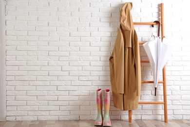 Photo of Umbrella, raincoat and rubber boots near white brick wall. Space for text