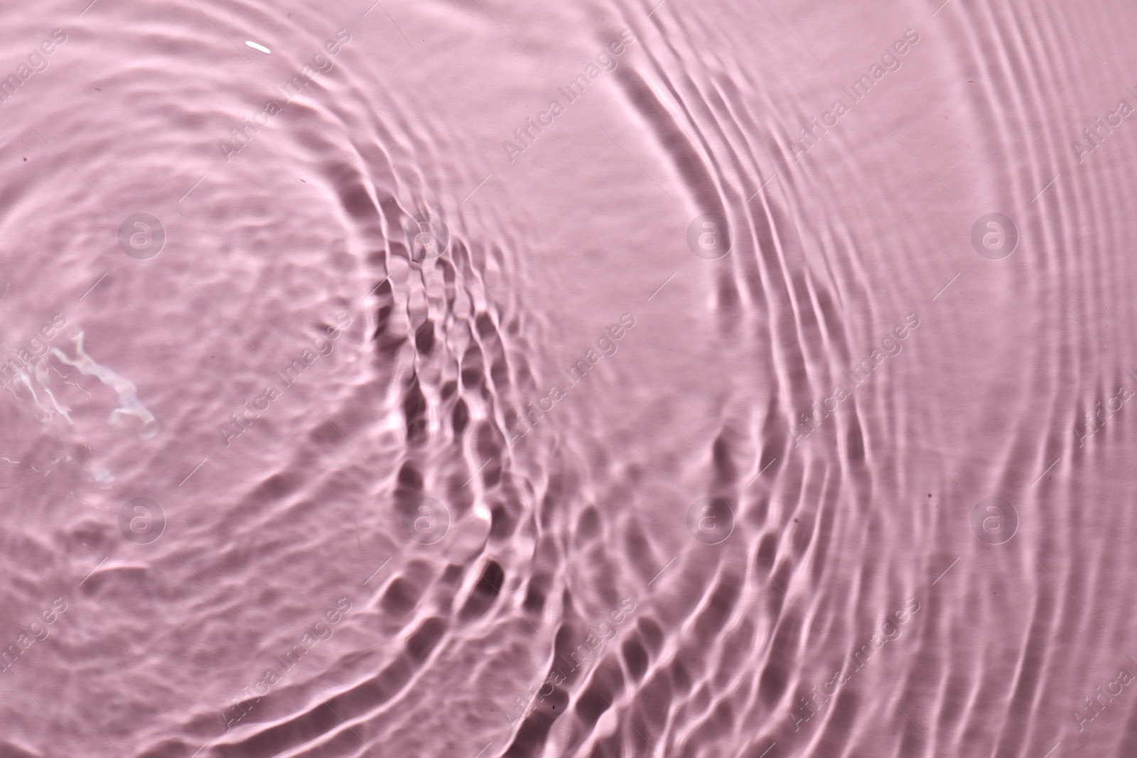 Photo of Rippled surface of clear water on pink background, top view