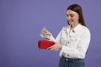 Happy woman putting money into wallet on purple background, space for text