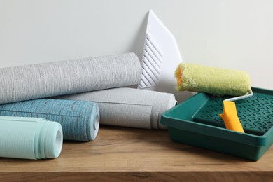 Photo of Different wallpaper rolls, roller and plastic spatula on wooden table