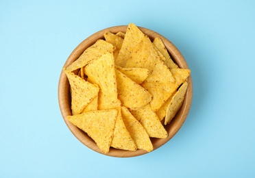 Wooden bowl with tasty Mexican nachos chips on light blue background, top view