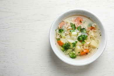 Photo of Bowl of fresh homemade vegetable soup on white wooden background, top view. Space for text