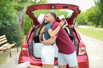 Beautiful young couple near car and suitcase packed for summer journey in trunk