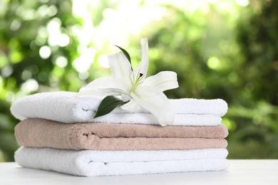 Photo of Stack of clean soft towels and flower on table against blurred background