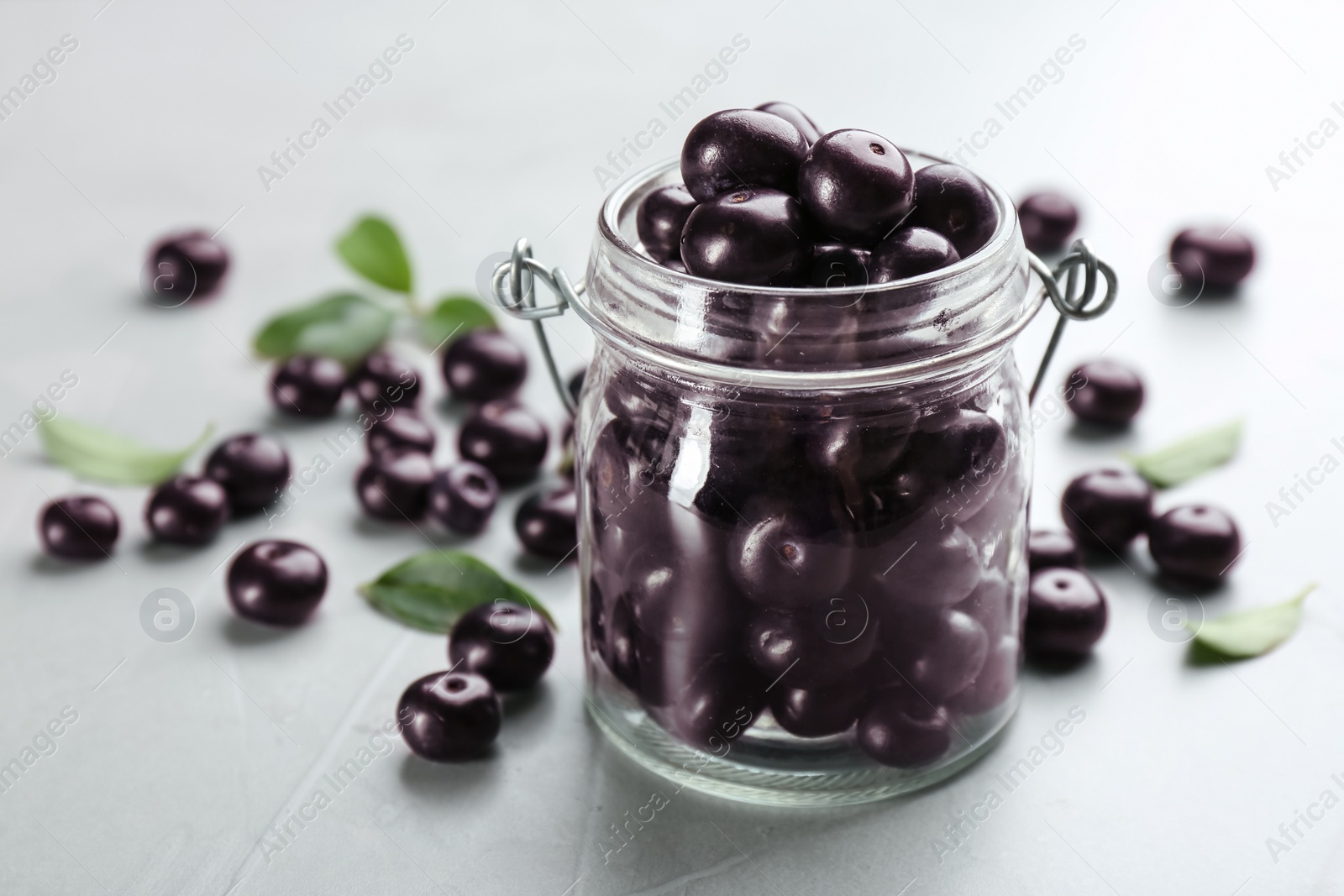 Photo of Fresh acai berries in glass jar on light grey table, closeup