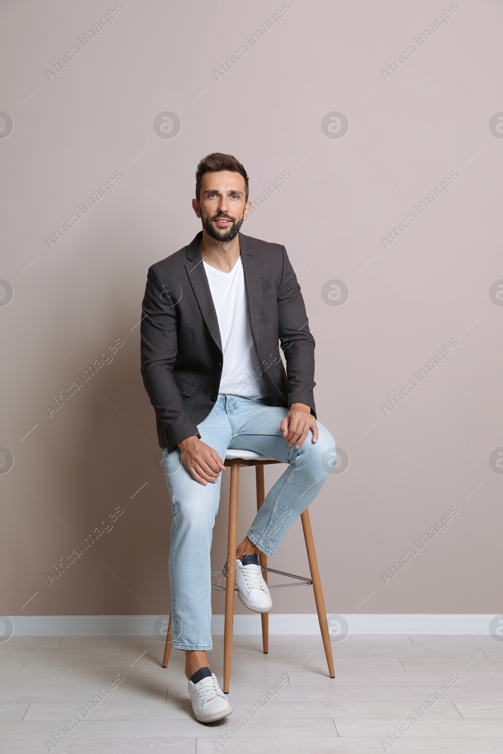 Photo of Handsome man sitting on stool near beige wall