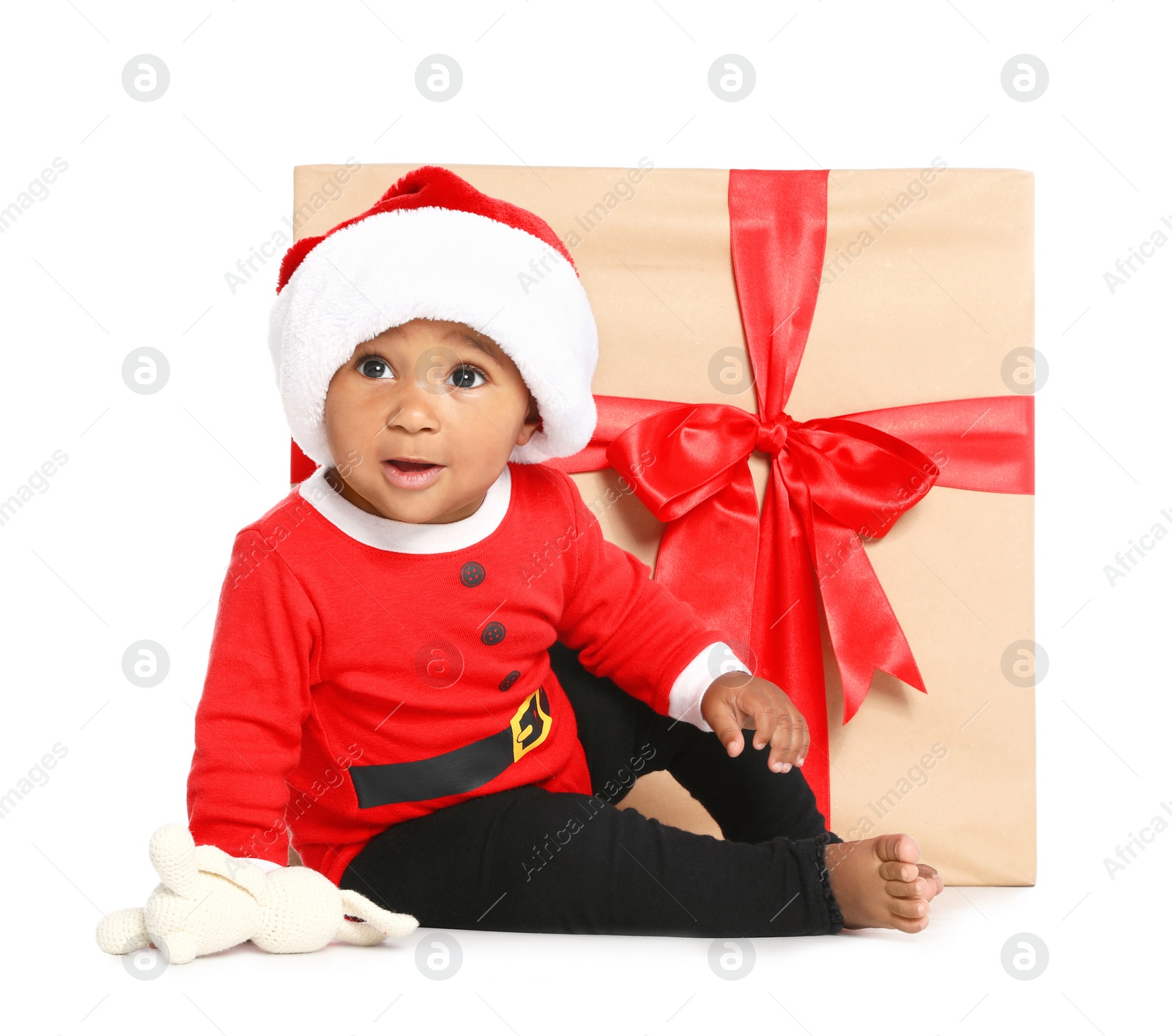 Photo of Festively dressed African-American baby with toy near Christmas gift on white background
