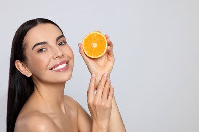 Photo of Woman holding half of orange on light grey background, space for text. Spa treatment