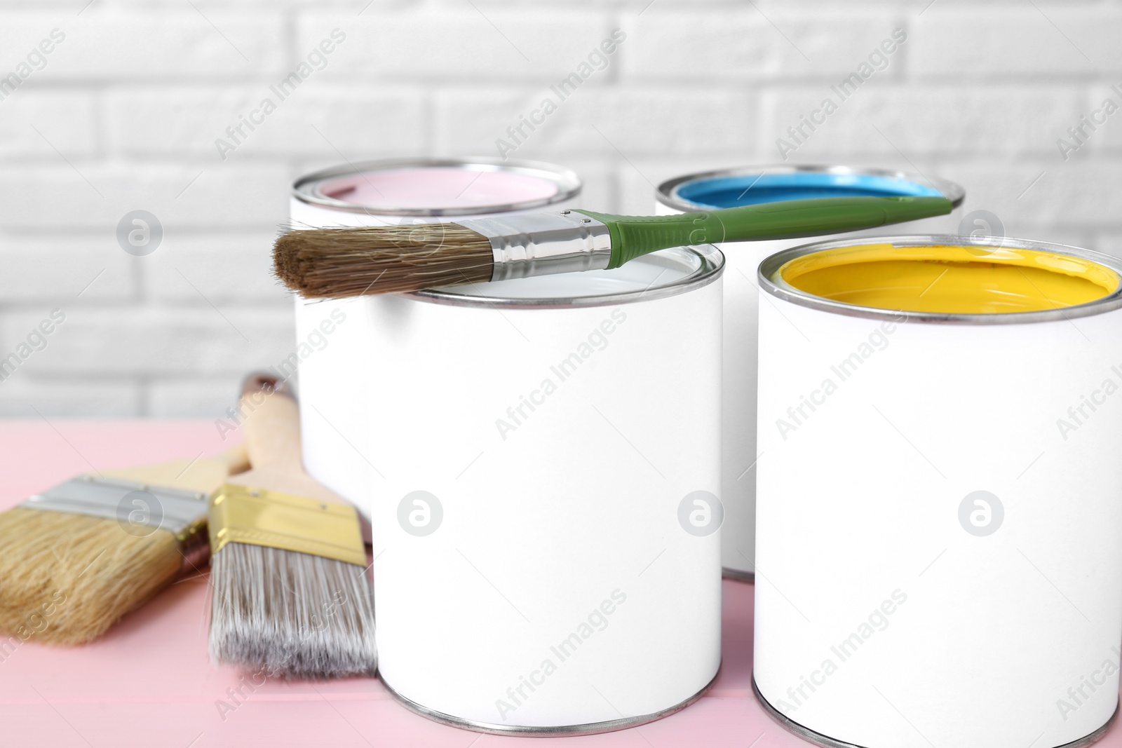 Photo of Cans of colorful paints and brushes on pink table, closeup