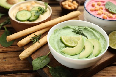 Photo of Bowl of delicious green hummus with rosemary, avocado and lime on wooden table