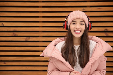 Photo of Young woman listening to music with headphones against wooden wall. Space for text