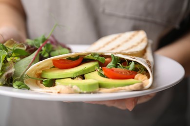 Photo of Woman holding plate with delicious hummus wraps and vegetables, closeup