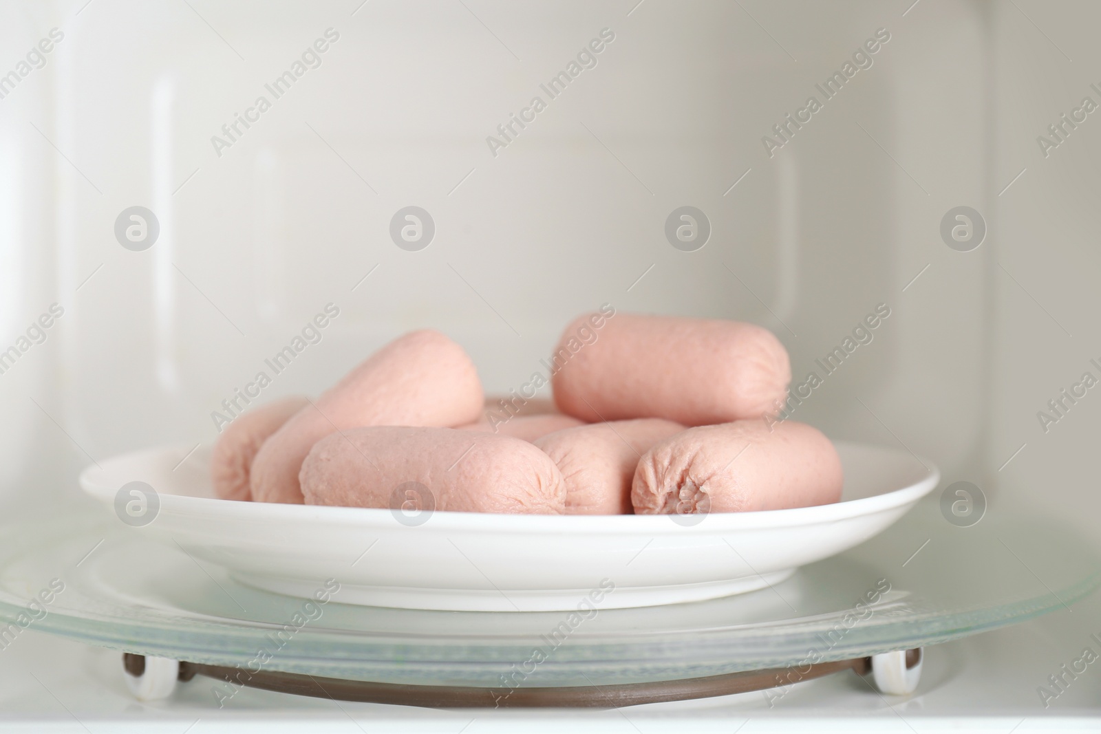 Photo of Tasty sausages on plate in microwave oven. Meat product