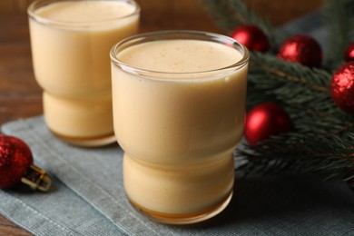 Photo of Glasses of delicious eggnog and decorated fir branch on wooden table, closeup