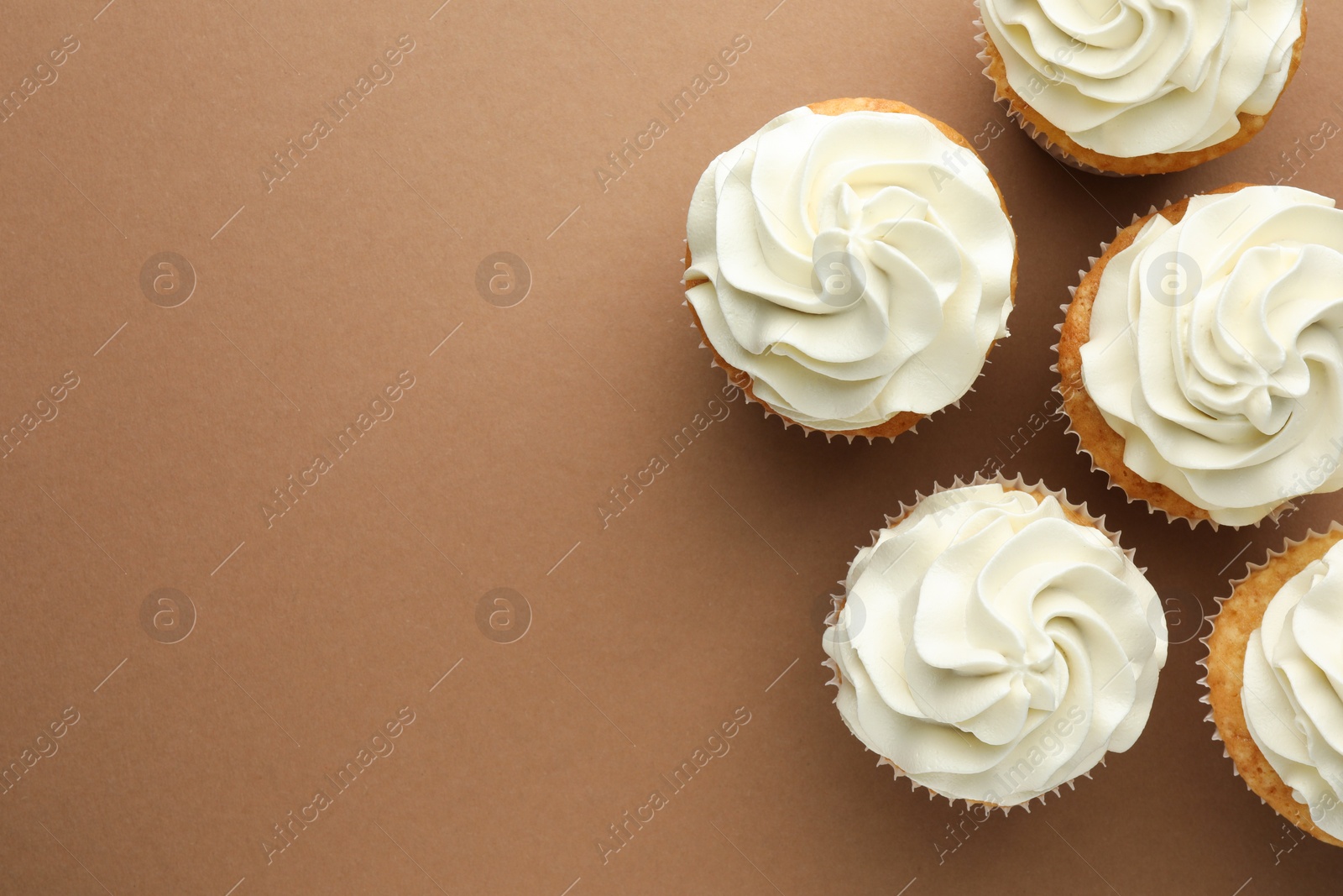 Photo of Tasty vanilla cupcakes with cream on dark beige background, top view. Space for text