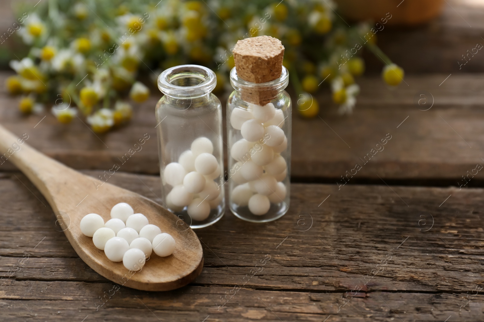 Photo of Bottles of homeopathic remedy and flowers on wooden table