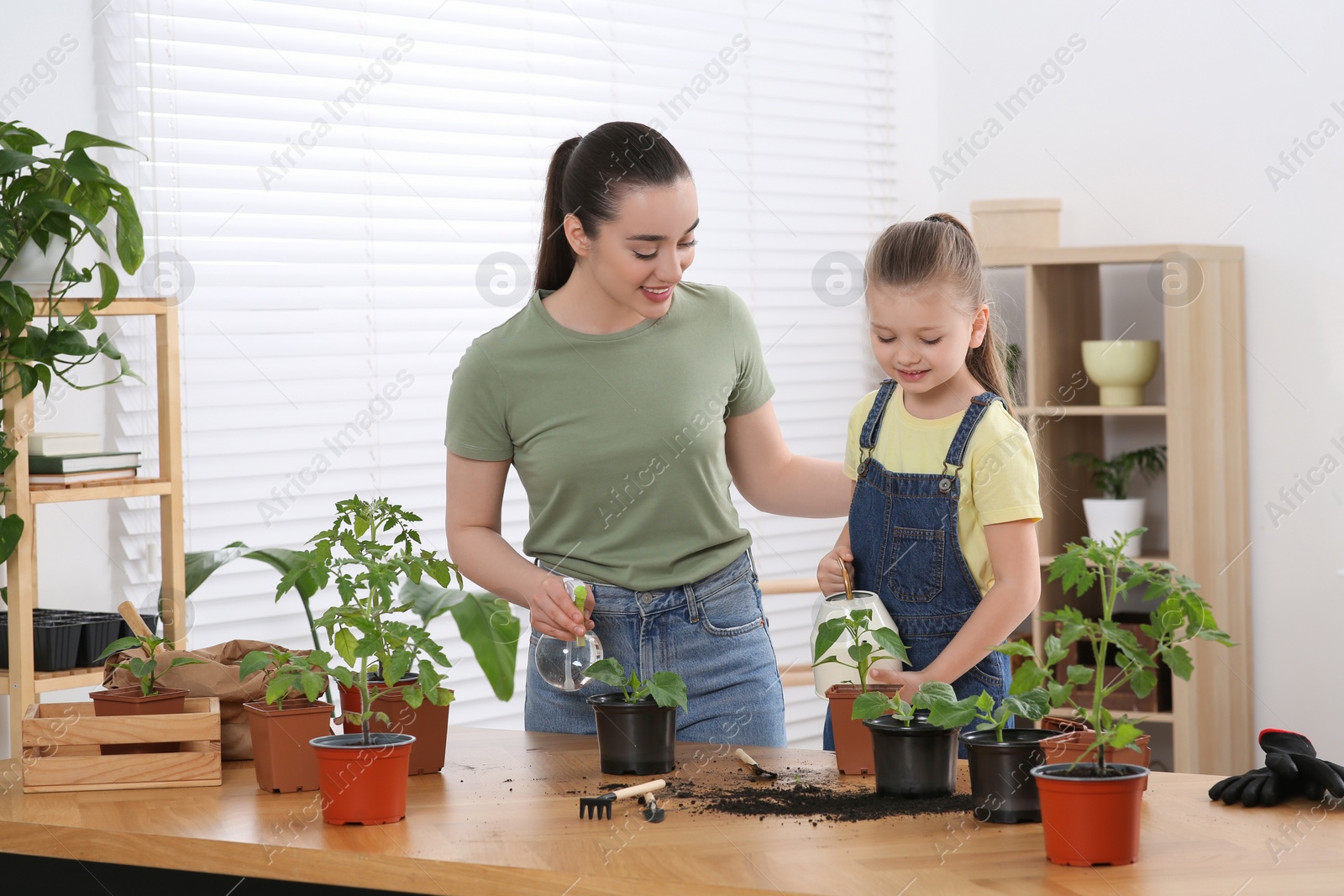 Photo of Mother and daughter taking care of seedlings together at wooden table in room