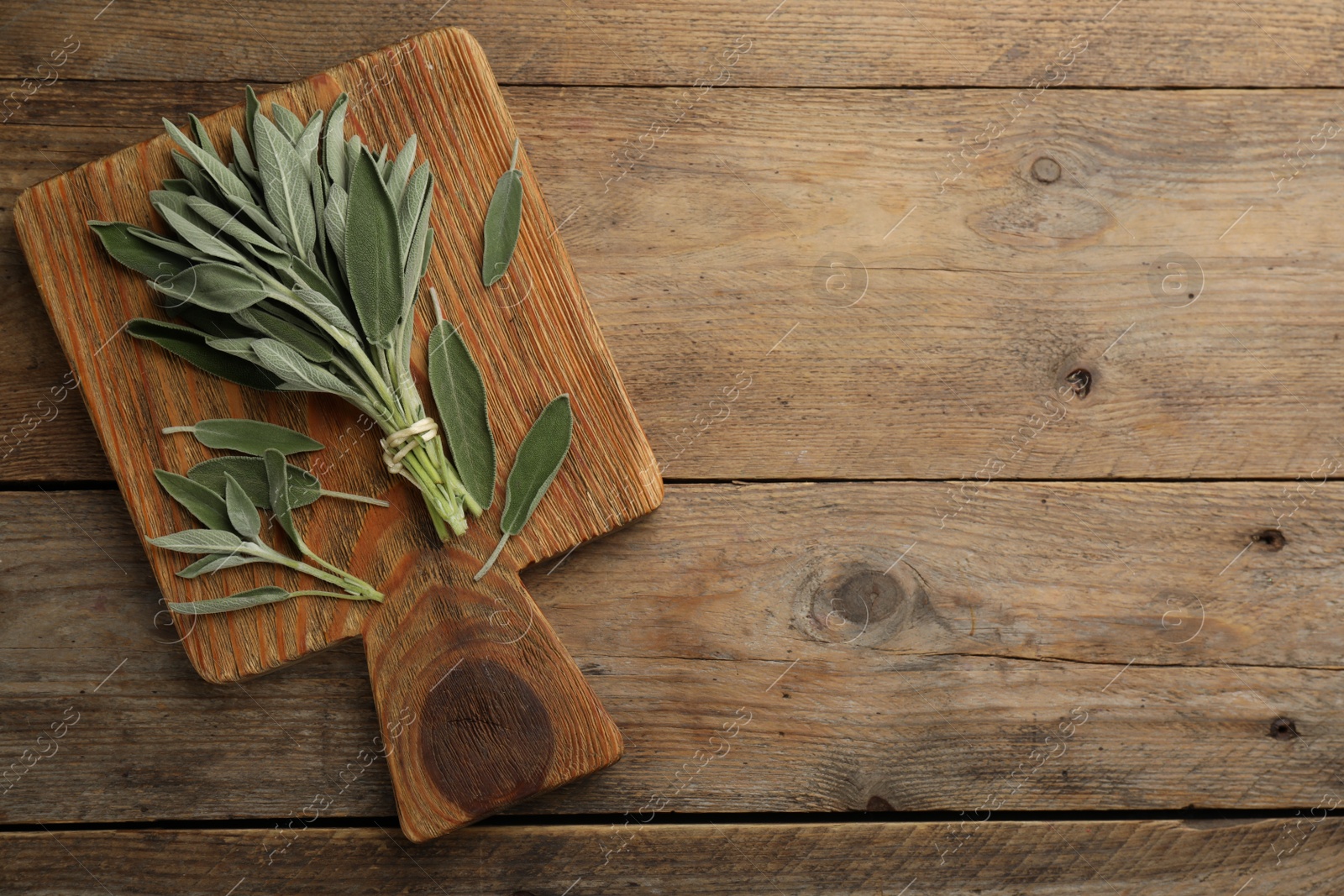 Photo of Board with fresh green sage on wooden table, top view. Space for text