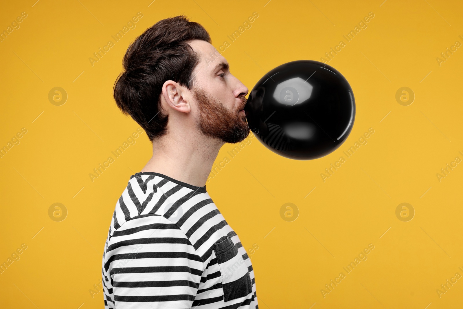 Photo of Man inflating black balloon on yellow background