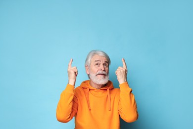 Photo of Senior man with mustache pointing at something on light blue background