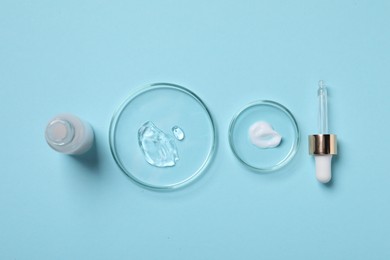 Photo of Petri dishes with samples of cosmetic serums, bottle and pipette on light blue background, flat lay