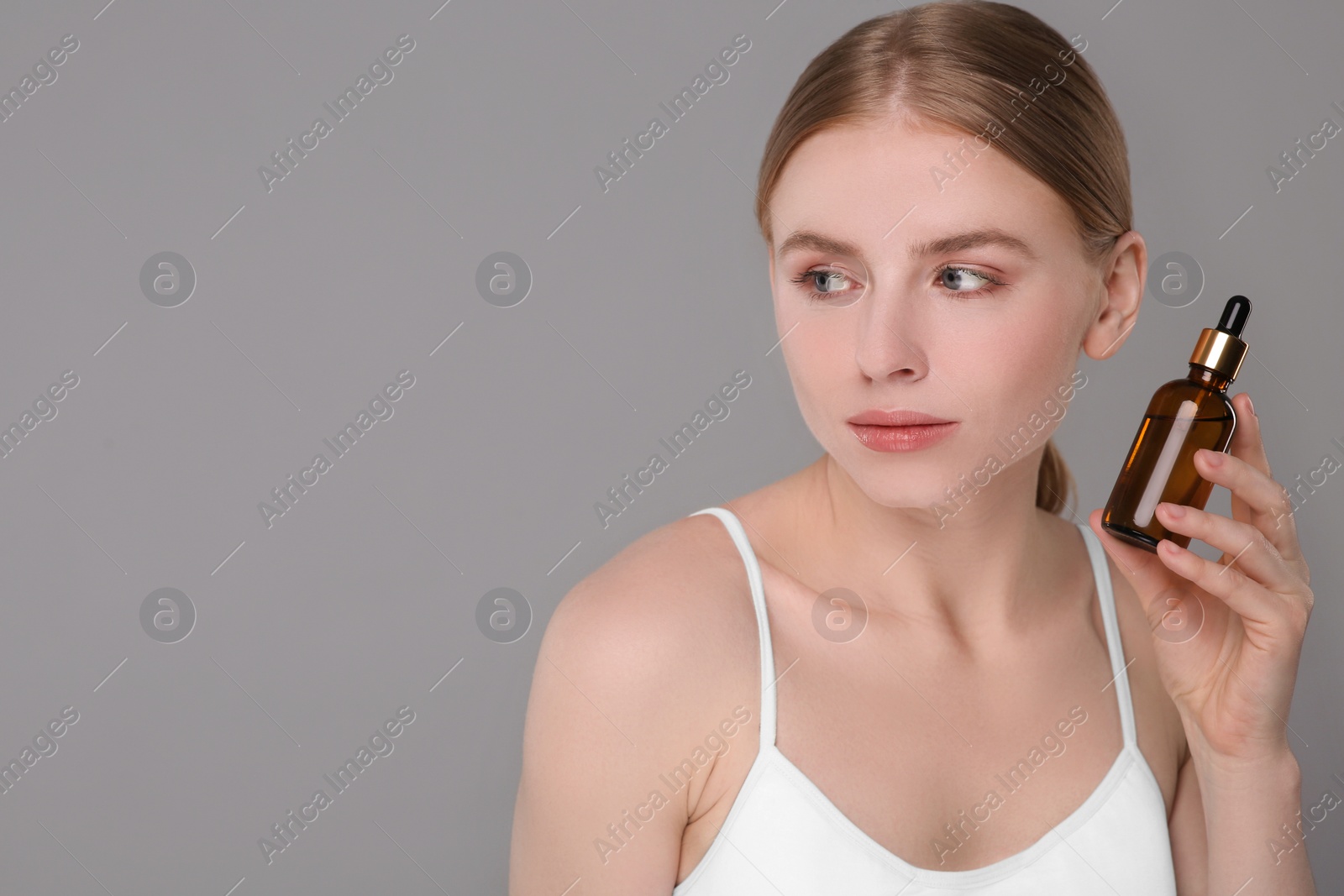 Photo of Beautiful young woman with bottle of essential oil on light grey background. Space for text