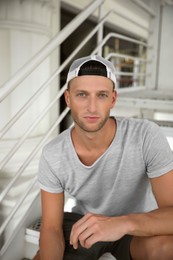 Photo of Handsome young man in stylish cap sitting on stairs outdoors