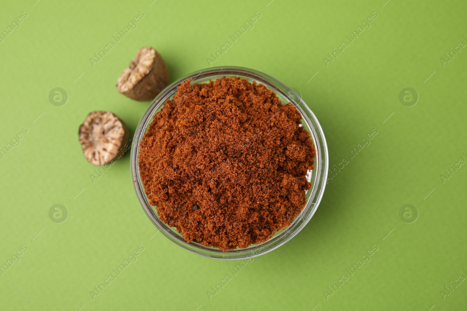 Photo of Nutmeg powder in bowl and halves of seed on light green background, flat lay
