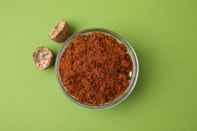 Nutmeg powder in bowl and halves of seed on light green background, flat lay