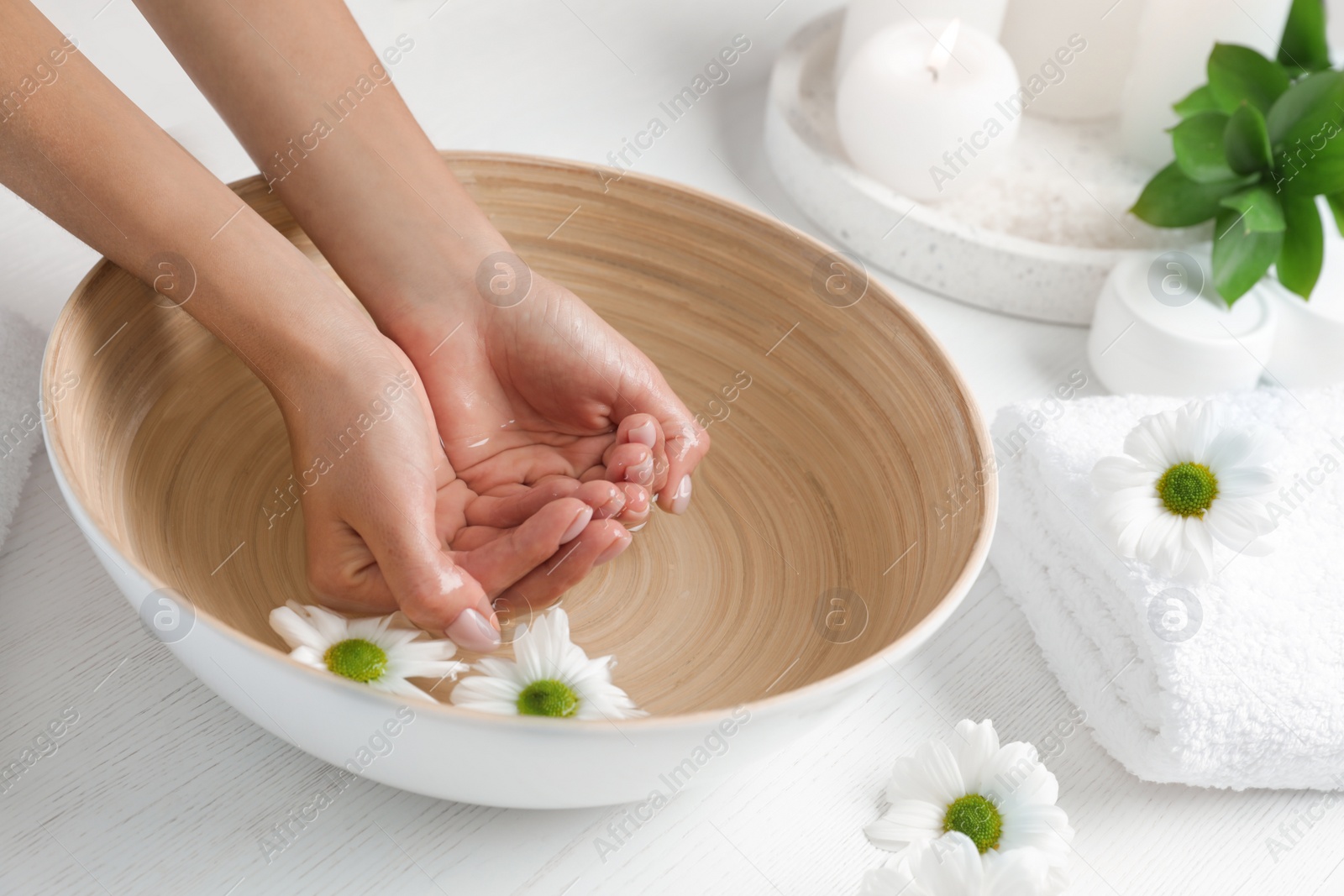 Photo of Woman soaking her hands in bowl of water and flowers on table, closeup with space for text. Spa treatment