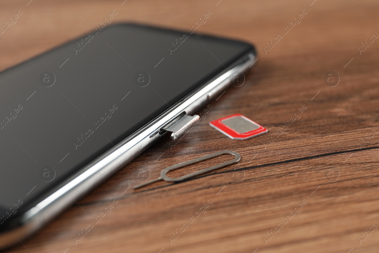 Photo of Mobile phone, SIM card and ejector tool on wooden table, closeup